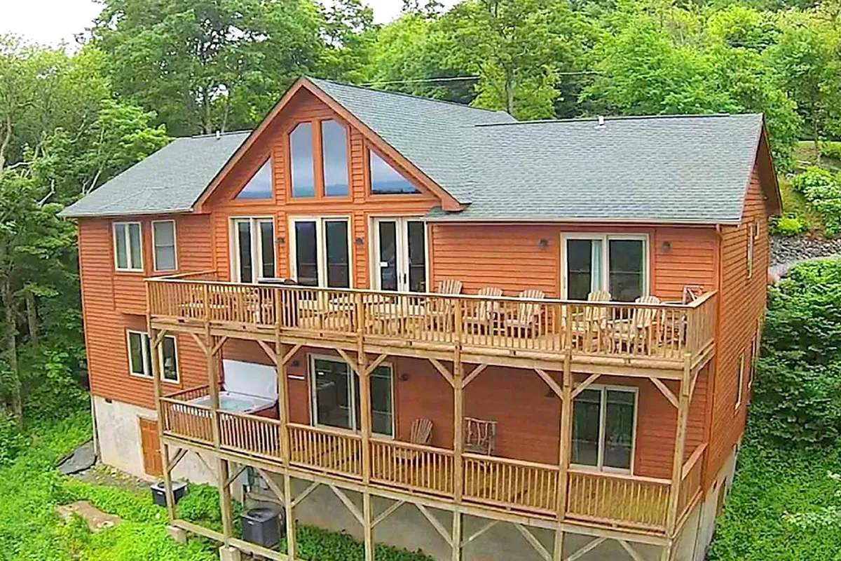 A large wooden deck surrounds the home, featuring expansive windows that look into the living spaces. The deck is bordered by lush greenery, offering both privacy and a connection to nature. The space is ideal for gatherings, morning coffee, or evening chats.