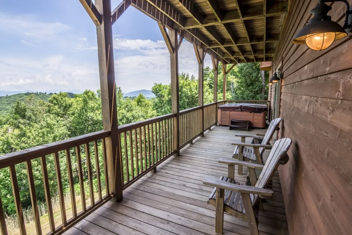 A spacious deck with Adirondack chairs and a hot tub overlooks sweeping mountain views. The space is perfect for relaxing after a day of skiing or hiking, with railings framing a tranquil, immersive outdoor experience.