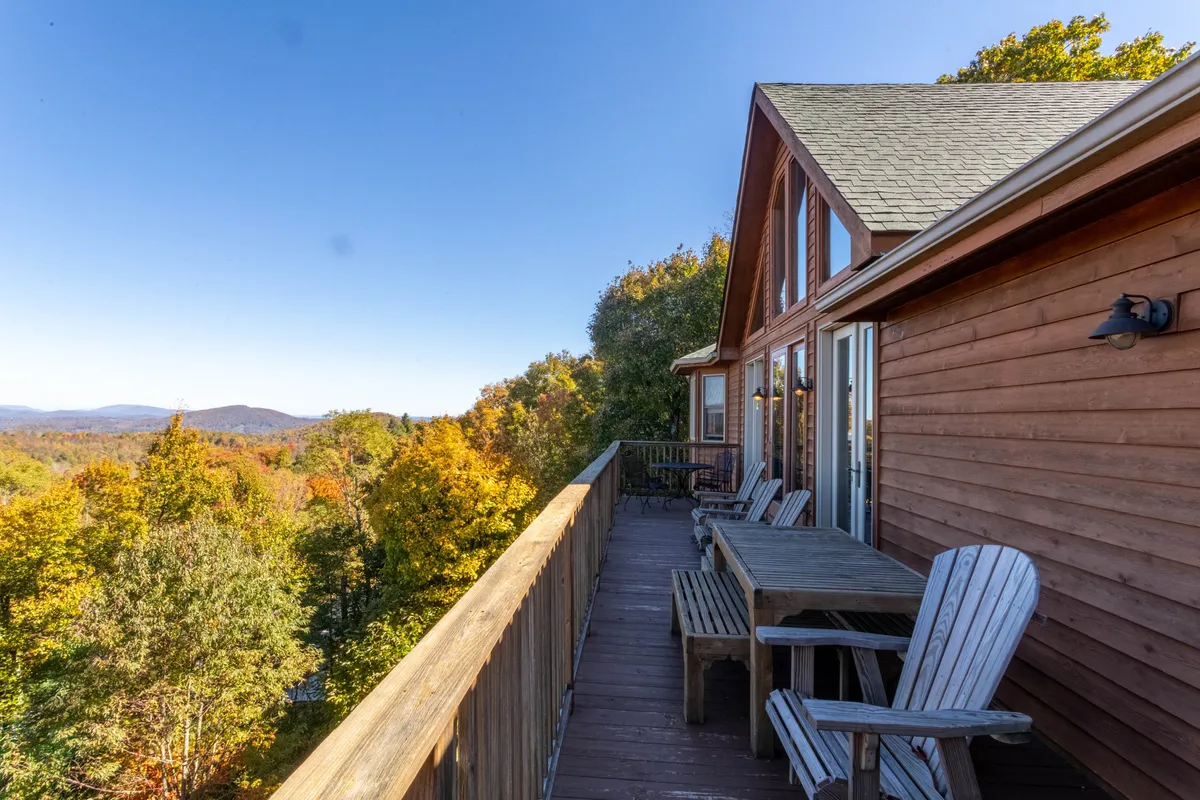 A spacious wooden deck furnished with comfortable outdoor seating, overlooking a stunning panoramic mountain view. The scene suggests a peaceful place to relax outdoors, surrounded by nature's beauty.