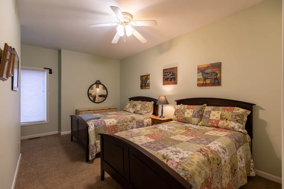A flexible guest bedroom featuring two beds with patterned quilts, a round mirror, nightstand with lamp, and framed artwork. The cozy atmosphere is suitable for children or adults alike.