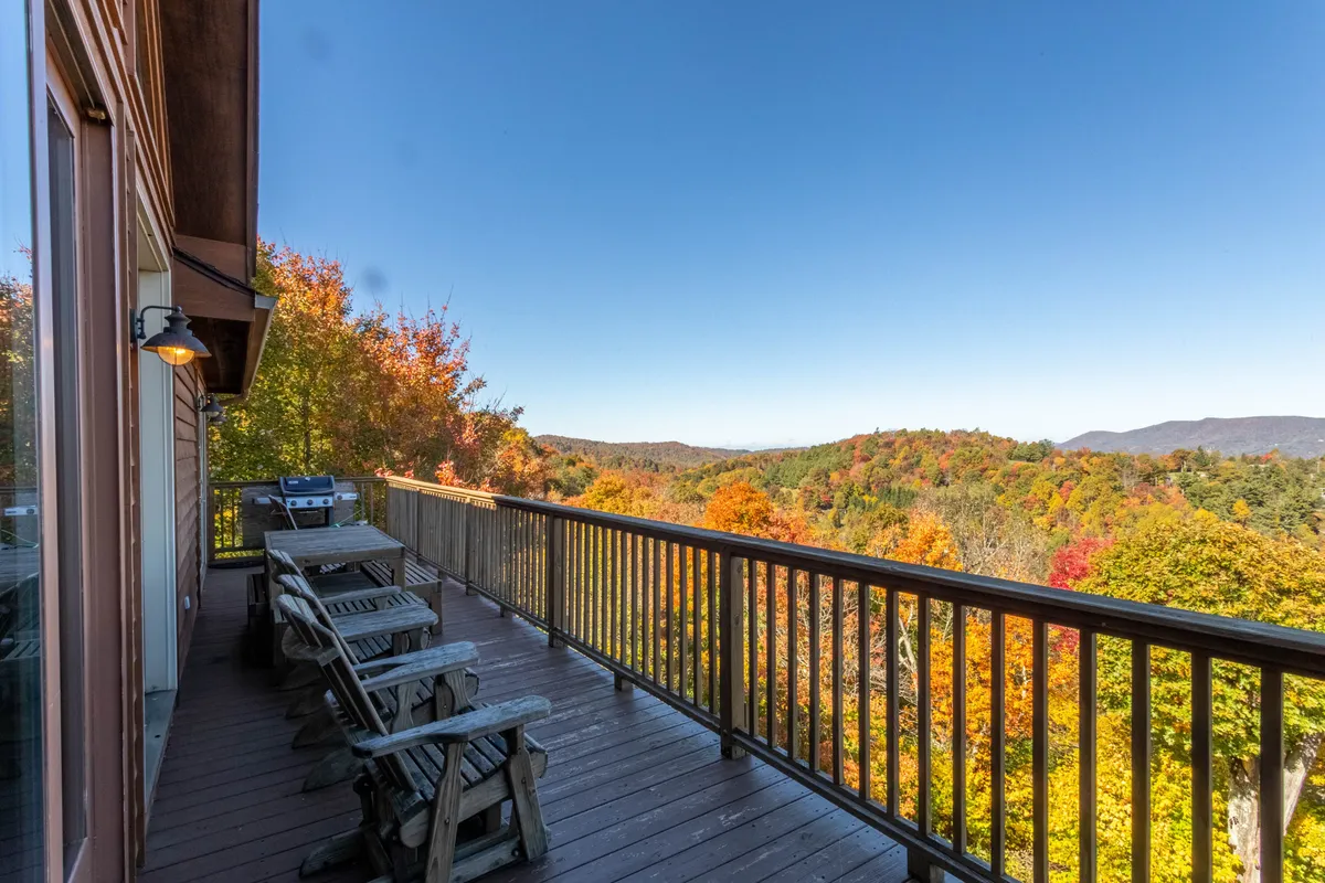 A wooden deck overlooks breathtaking mountain views and vivid autumn foliage. Comfortable outdoor seating invites relaxation, while the deck itself offers a safe, contained space for pets to join in the mountain air and scenery. The backdrop of forested hills illustrates the proximity to nature trails.