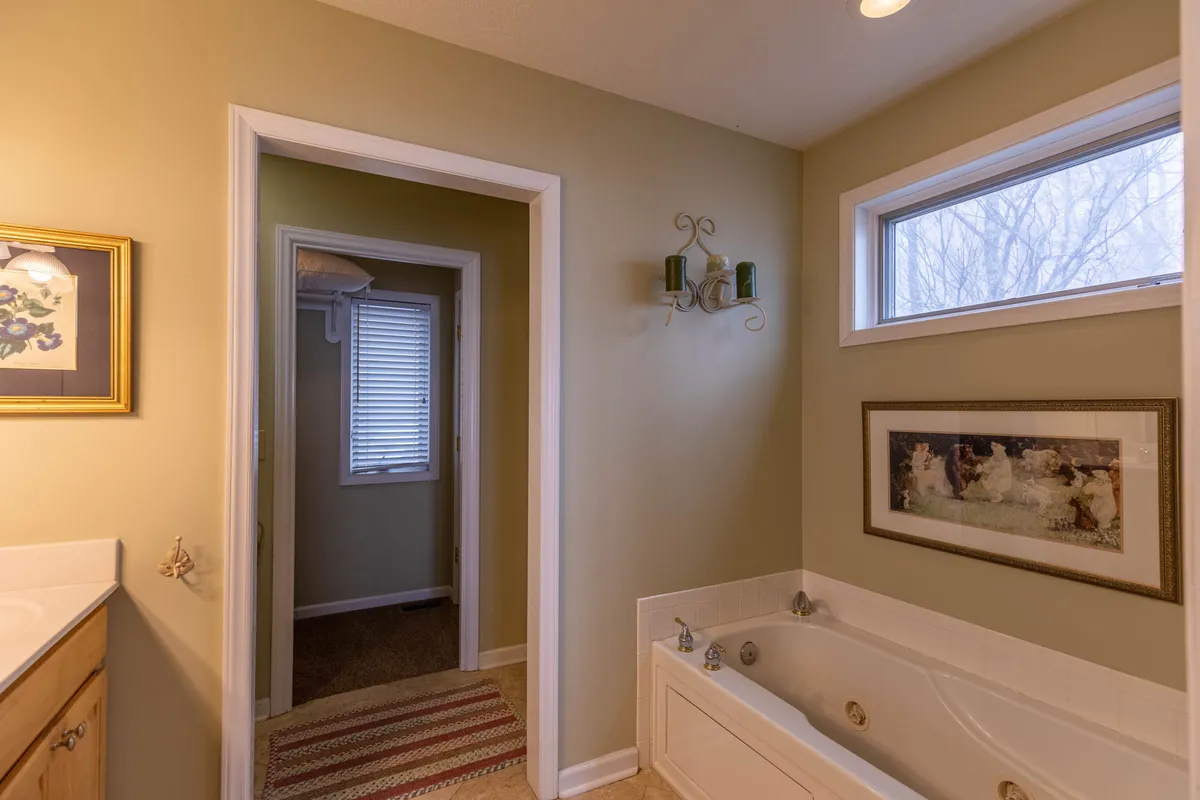 A peaceful bathroom with a standalone bathtub, framed artwork, window, and inviting ambiance. Natural light streams in, creating a soothing space ideal for evening relaxation.