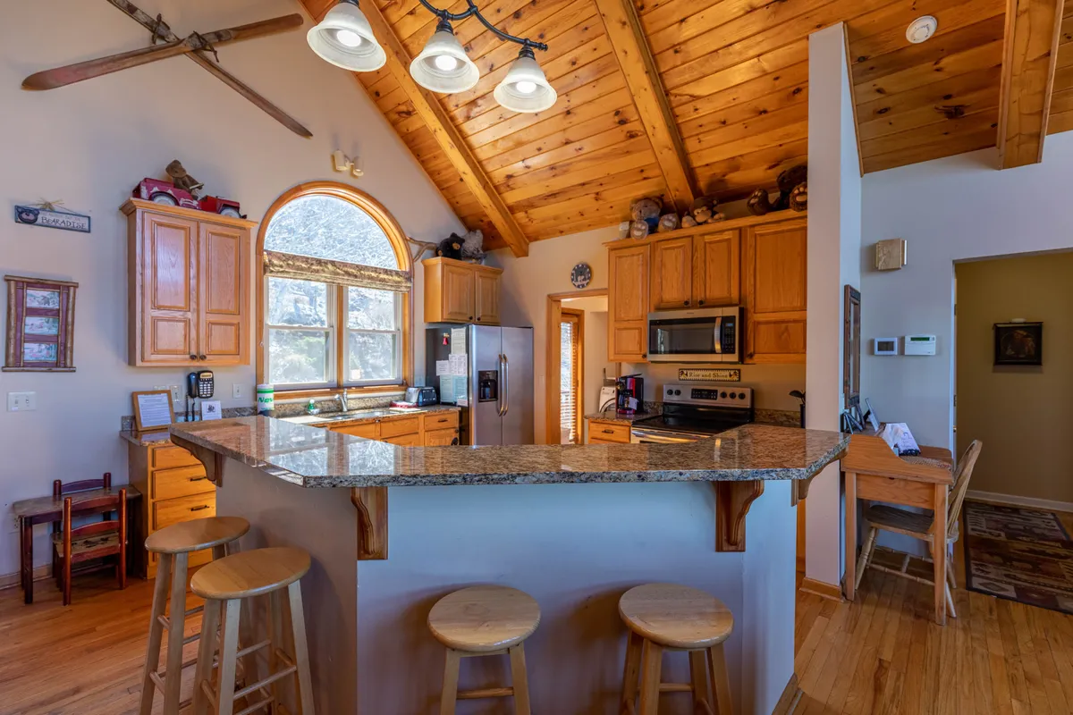 A close-up of the gourmet kitchen featuring gleaming granite countertops, wooden cabinetry, arched windows, and cozy bar seating with stools. The inviting setup evokes scenes of meal preparation, casual breakfasts, and festive holiday cooking.