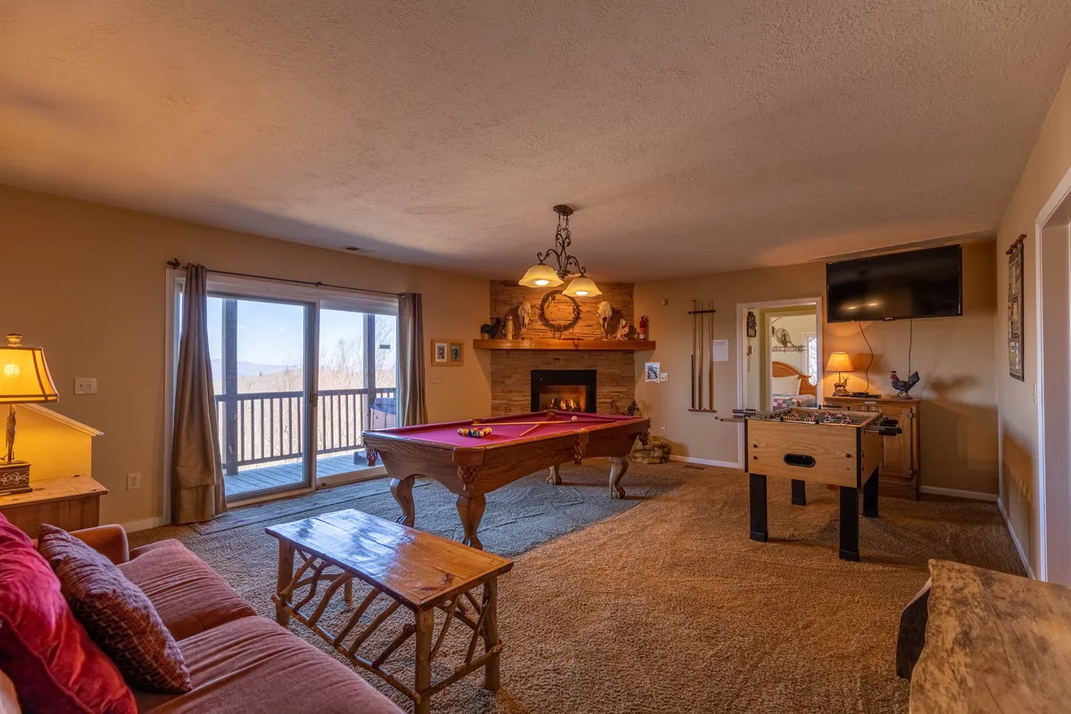 A friendly game room environment with both a pool table and a foosball table, arranged near a fireplace and a comfortable sofa. The overall setting encourages group activities and relaxation, ideal for movie nights or tournaments. The TV adds a multimedia entertainment element.