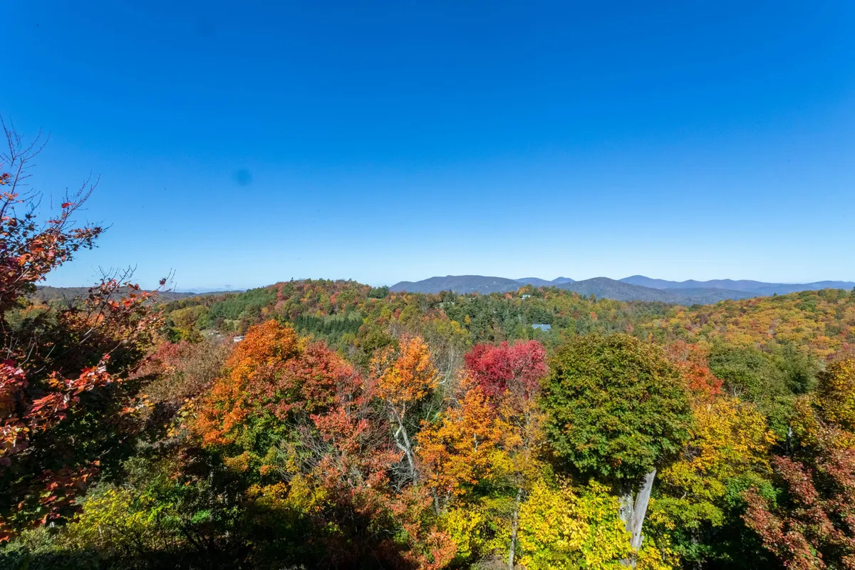 A scenic view of rolling distant mountains blanketed in vibrant autumn foliage under a clear blue sky. The image radiates tranquility and a deep connection to the surrounding natural landscape.